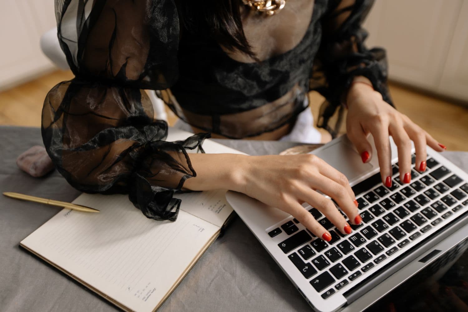 Hands typing on a laptop beside a notebook and pen